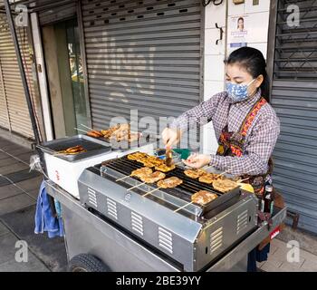 Bangkok, Thailandia - 28 febbraio 2020: Un tradizionale venditore di cibo di strada, che vende carne alla griglia su un bastone, in una strada di Bangkok. Foto Stock