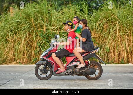 Una famiglia tailandese che viaggia su una moto, tutte indossando maschere facciali protettive, prese a Pathumthani, Thailandia, nel mese di aprile 2020. Foto Stock