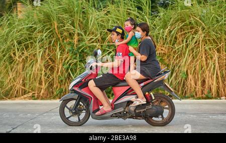 Una famiglia tailandese che viaggia su una moto, tutte indossando maschere facciali protettive, prese a Pathumthani, Thailandia, nel mese di aprile 2020. Foto Stock