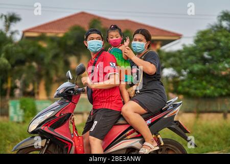 Una famiglia tailandese che viaggia su una moto, tutte indossando maschere facciali protettive, prese a Pathumthani, Thailandia, nel mese di aprile 2020. Foto Stock