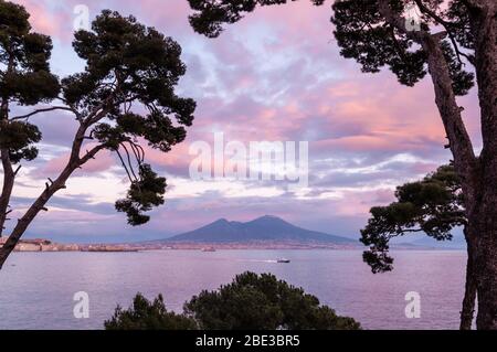 Vista attraverso gli alberi da Posillipo della bellissima città di Napoli, con un cielo meraviglioso con i colori del tramonto. Foto Stock