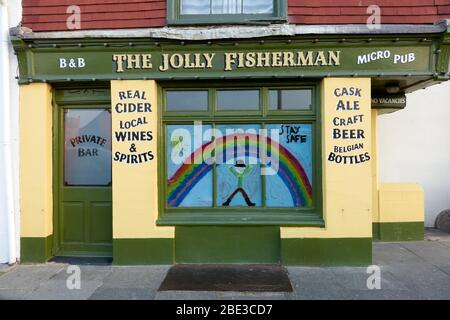 Il pub Jolly Fisherman di Hastings, chiuso durante il blocco del coronavirus, mostrando un arcobaleno dipinto in solidarietà, con un messaggio per rimanere al sicuro Foto Stock