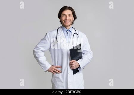 Esperto medico sorridente e sicuro con appunti che si posano su sfondo chiaro Foto Stock