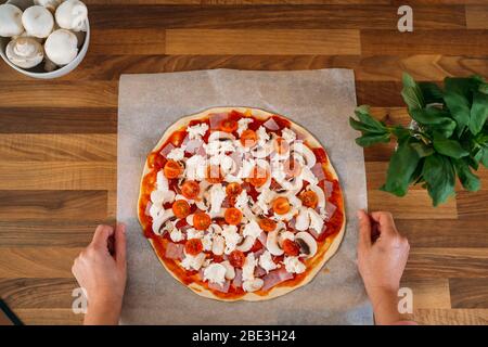 Vista dall'alto di una donna che prepara una pizza tradizionale italiana fatta in casa margherita. Preparazione classica pizza italiana su piano di lavoro in legno Foto Stock