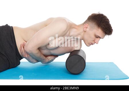 Il bell'uomo mostra esercizi, utilizzando un rullo in schiuma per un massaggio miofasciale sul tappetino da ginnastica in studio. Isolato su bianco. Foto Stock