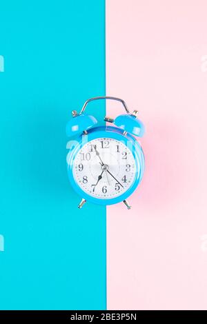 Sveglia classica con due campanelli, isolata su sfondo geometrico colorato blu e rosa pastello. Ore di riposo tempo di vita buona mattina notte sveglia Foto Stock