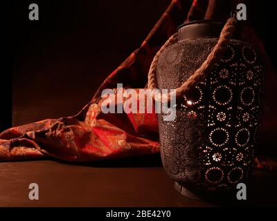 Lanterna araba vicino a un tessuto rosso orientale su uno sfondo di legno marrone.lampada Eid o lanterna per Ramadan e altre vacanze islamiche musulmane, con copia Foto Stock