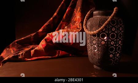 Lanterna araba vicino a un tessuto rosso orientale su uno sfondo di legno marrone.lampada Eid o lanterna per Ramadan e altre vacanze islamiche musulmane, con copia Foto Stock