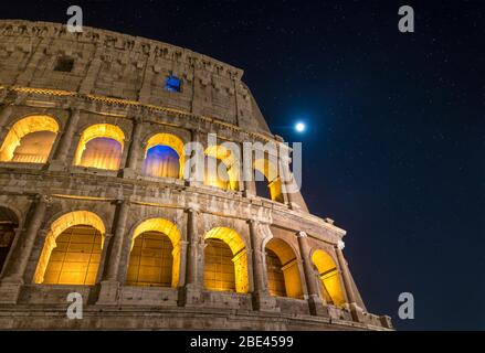 Colosseo Romano che illumina di notte sotto una luna piena e uno stellare luminoso a Roma, Italia Foto Stock