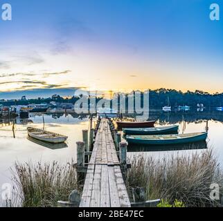 Tradizionali barche in legno ormeggiate ad un molo di legno sul Porto di Macquarie con la città di Strahan attraverso la baia sullo sfondo. Foto Stock