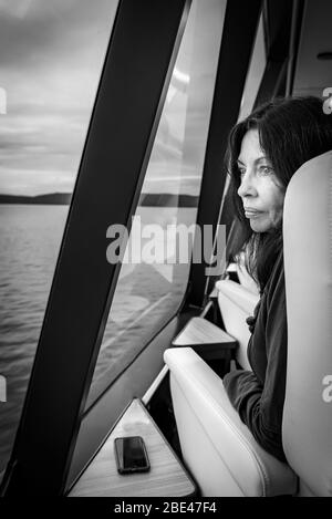 Profilo bianco e nero di una turista femminile che guarda fuori dalla finestra a bordo della barca Gordon River Cruise lasciando Strahan in Tasmania. Foto Stock