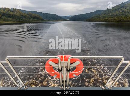 Una vista attraverso le ringhiere di poppa in acciaio inossidabile e la boa arancione di una barca da crociera sul fiume Gordon lungo il fiume Gordon. Foto Stock