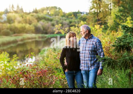 Una coppia matura che gode di un tempo di qualità insieme mentre cammina in un parco cittadino in una calda serata autunnale vicino al tramonto; St. Albert, Alberta, Canada Foto Stock