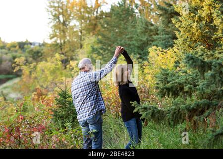 Una coppia matura godendo di tempo di qualità e ballando insieme mentre camminando lungo un fiume in un parco cittadino su un calda serata d'autunno Foto Stock