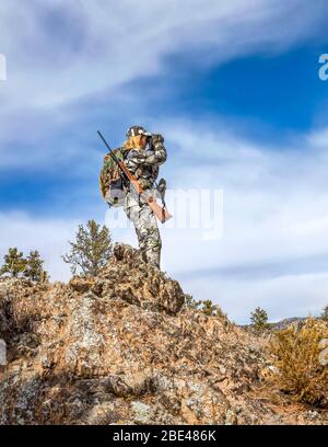 Hunter con camouflage abbigliamento e fucile guardando fuori con binocolo; Denver, Colorado, Stati Uniti d'America Foto Stock