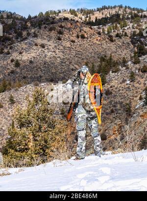 Hunter con camouflage abbigliamento e fucile guardando fuori con binocolo in inverno; Denver, Colorado, Stati Uniti d'America Foto Stock