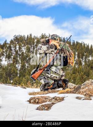 Hunter con camouflage abbigliamento e fucile guardando fuori con binocolo; Denver, Colorado, Stati Uniti d'America Foto Stock