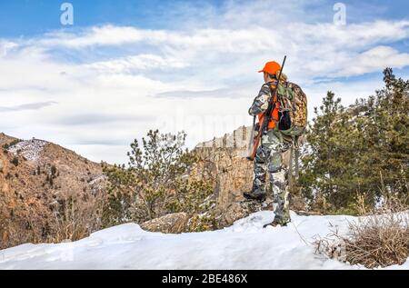 Hunter con camouflage abbigliamento e fucile guardando fuori in inverno; Denver, Colorado, Stati Uniti d'America Foto Stock