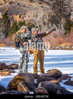 Cacciatori con abiti da camuffamento e fucile che si affaccia con binocoli; Denver, Colorado, Stati Uniti d'America Foto Stock