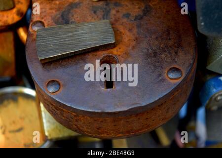 Primo piano di un lucchetto arrugginito con altre serrature metalliche sullo sfondo. Simbolo per gli amanti, mistero, segreto e chiave. Foto Stock