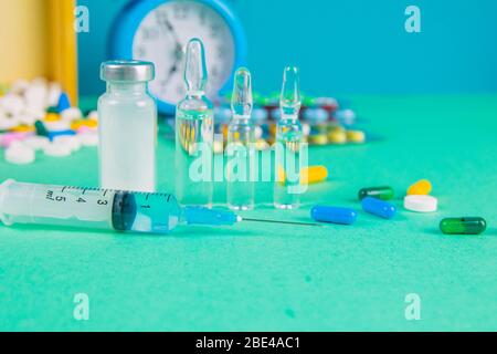 Siringa con flaconcini di vetro e farmaci pillole farmaco. Sullo sfondo si trova una scatola di legno e una mela gialla. Vista frontale Foto Stock