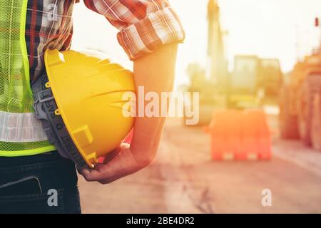 Ingegnere che tiene il casco nel cantiere stradale con informazioni generali sui macchinari, concetto di sicurezza Foto Stock