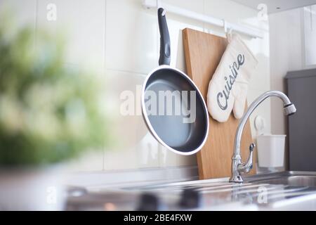 Accessori da cucina appesi nella barra portatutto sulla parete bianca Foto Stock