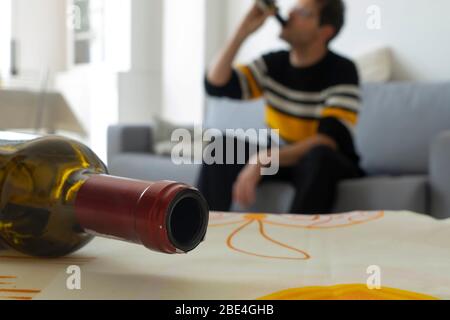L'uomo alcolico si ubriaca sul divano a casa sullo sfondo. Bottiglia di vino vuota in primo piano. Concetto di dipendenza da alcol. Foto Stock