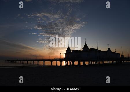 Ahlbeck, Germania. 12 aprile 2020. Le nuvole si muovono nelle prime ore del mattino durante l'alba nel cielo sopra il molo sull'isola di Usedom. Il molo lungo 280 m è stato aperto nel 1898 ed è il più antico della Germania. Credit: Stefan Sauer/dpa/Alamy Live News Foto Stock