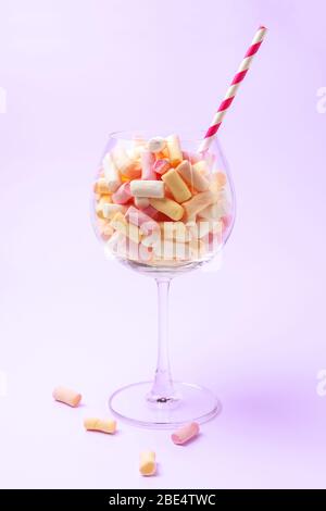 Mini marshmallows in vetro su sfondo viola chiaro. Marshmallow multicolore in un vetro. Concetto dolciario. Primo piano dello spazio di copia Foto Stock