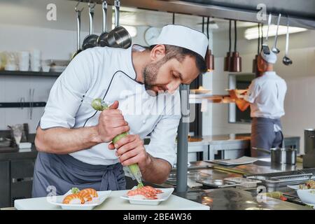 Chef che prepara sushi al ristorante. Si concentra sull'aggiunta di pasta wasabi ai sushi giapponesi tradizionali serviti su un piatto di pietra bianca. Concetto di cucina. Vista laterale Foto Stock