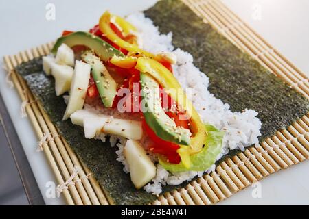 Sushi ingredienti, nori alghe makisu sul tappetino di bambù per  laminazione, crudo fresco salmone, materie di riso sushi, la salsa di soia  e bacchette sul lato Foto stock - Alamy