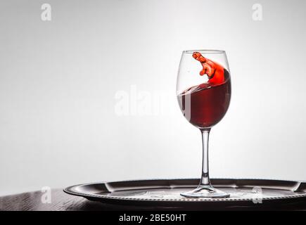 il vino rosso fuoriesce da un bicchiere che si trova in primo piano sul tavolo di legno Foto Stock