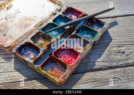 Palette di vecchie pitture miste con un pennello giace su un vecchio tavolo di legno grigio Foto Stock