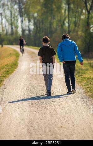 Madre e Figlio camminano su un sentiero vicino alla foresta con l'uomo che si avvicina in bicicletta, durante il blocco in Germania Foto Stock