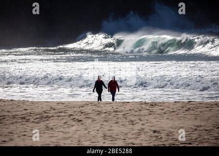 Due persone in silhouette fare una passeggiata lungo una spiaggia di sydney durante COVID 19 coronavirus pandemic per ottenere il loro esercizio quotidiano, Sydney, Australi Foto Stock