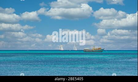 Barca da pesca bianca e gialla e due barche a vela bianche sul mare blu calmo Foto Stock