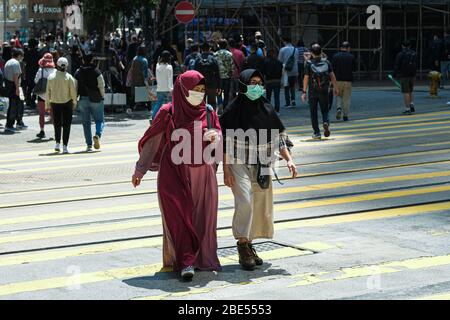 Hong Kong, Cina. 12 aprile 2020. Le persone indossano una maschera chirurgica per il viso mentre attraversano la strada. Corona Virus (Covid19) casi a Hong Kong hanno raggiunto oltre 1,000 il sabato, come le autorità hanno esortato il pubblico a rimanere a casa durante il lungo weekend di Pasqua. Credit: Keith Tsuji/ZUMA Wire/Alamy Live News Foto Stock