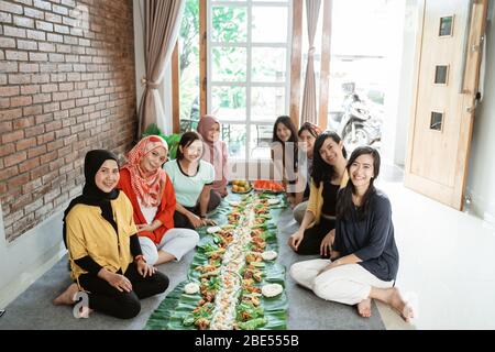 kembulan. amici di donna sorridenti guardando la macchina fotografica mentre pranzano insieme. tradizione asiatica giavanese mangiare insieme seduto sul pavimento Foto Stock