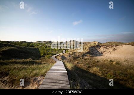 Passeggiata costiera costeggiando tra dune di sabbia vegetate con erba selvatica e macchia alla luce della sera o del mattino presto con un bagliore all'orizzonte Foto Stock