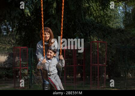 Madre che spinge il figlio sulle oscillazioni. Foto Stock