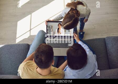 Medico online. I colloqui con la famiglia sono felici e si consultano con un medico che utilizza un computer portatile mentre si è seduti a casa sul divano. Foto Stock