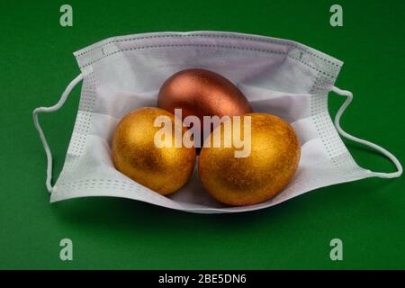 Pasqua 2020 immagine concettuale con uova di pasqua dorate in maschera medica protettiva. Annullamento della celebrazione concetto coronavirus pandemico. Antivirale m Foto Stock