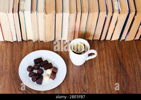 tazza di tè e caramelle al cioccolato su piastra bianca, stack di vecchio libro su tavola di legno, educazione concept background, molti libri pile con spazio copia per Foto Stock