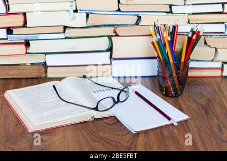 Libro di testo aperto, notebook, occhiali, matite nel supporto, stack di vecchio libro su tavola di legno, istruzione concetto di fondo, molti libri pile con spazio di copia Foto Stock