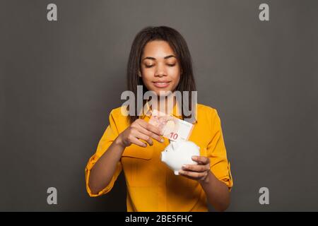 Intelligente donna nera di successo che mette in Piggy banca dieci banconote euro Foto Stock