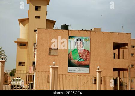 Guarda un poster sul muro con la figura dell’ex presidente libico, ora morto, Muhammar Quaddafi Foto Stock