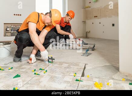 Due lavoratori stanno installando piastrelle di ceramica sul pavimento. Foto Stock