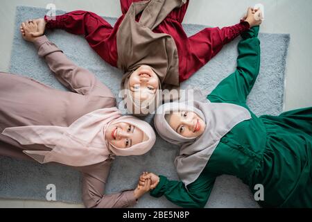gruppo di amici mussulmani sorrise mentre si posava sul materasso e tendeva le mani a guardare Foto Stock