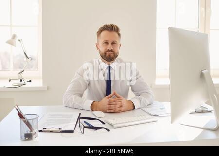 Uomo d'affari serio occupato in una camicia bianca che lavora seduto ad un tavolo con un computer in ufficio. Foto Stock